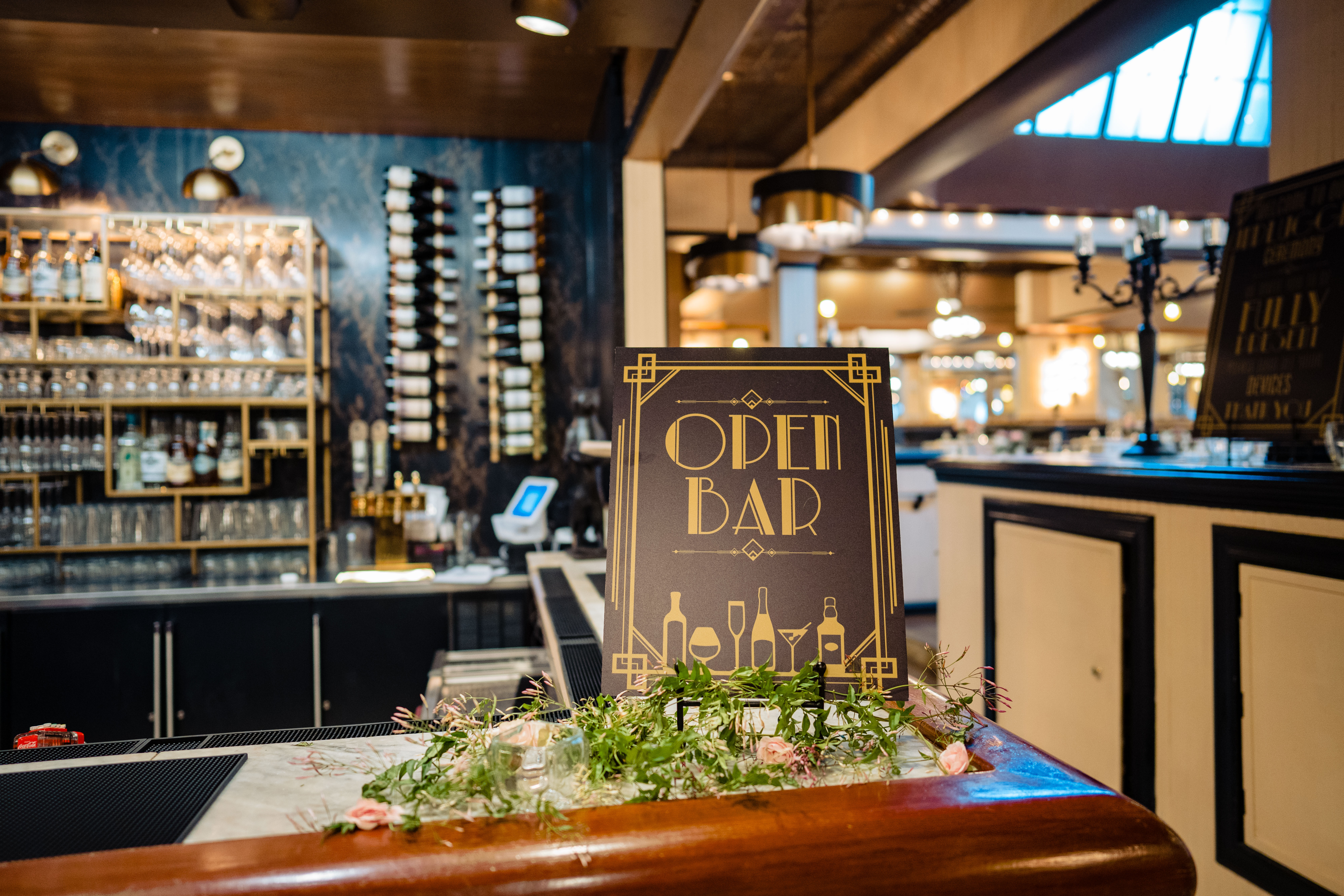 An art-deco style open bar sign with greenery laid around it