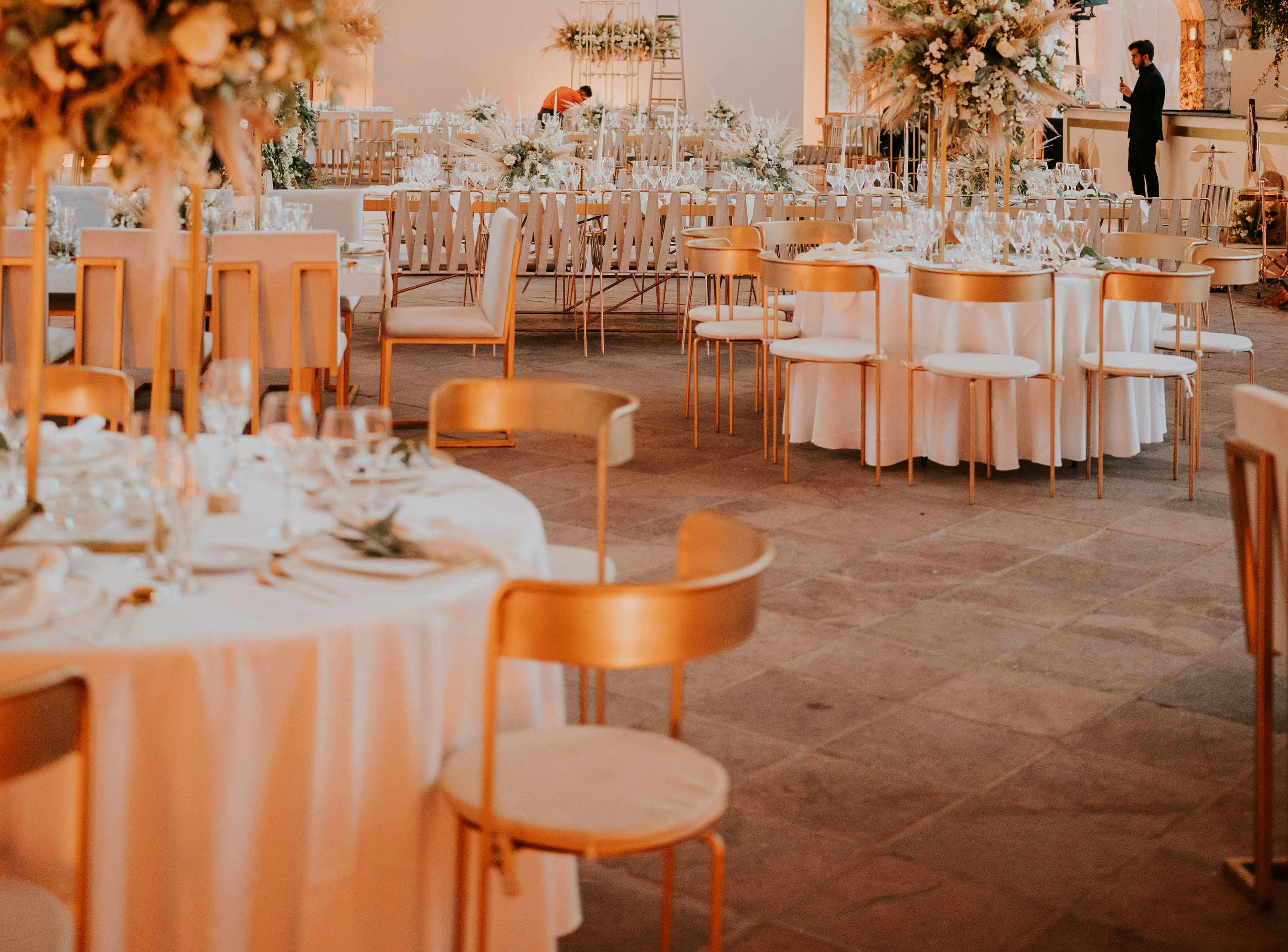 Wedding venue set with white linens and upscale gold chairs.