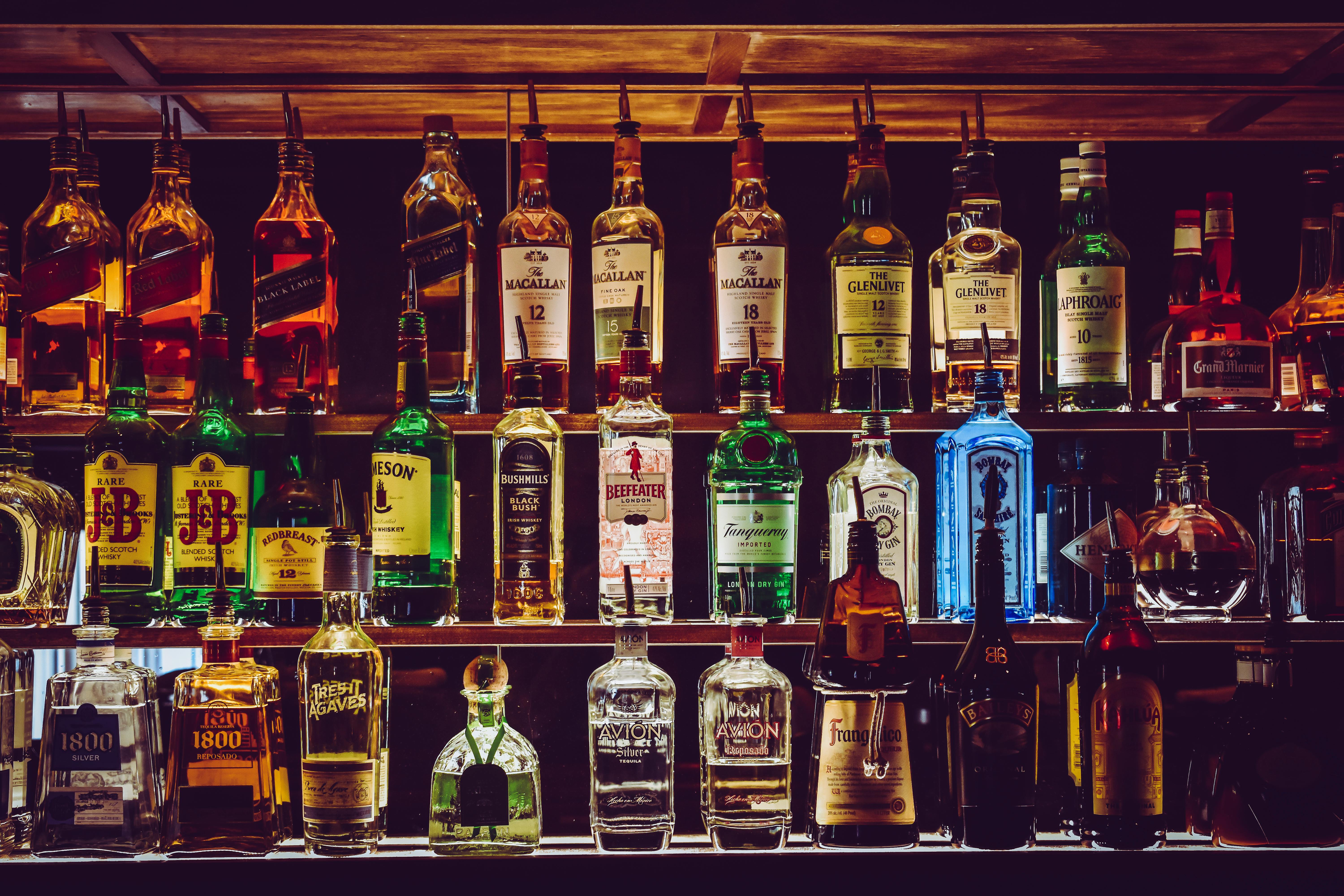 A backlit bar shelf with many colorful glass bottles of liquor.