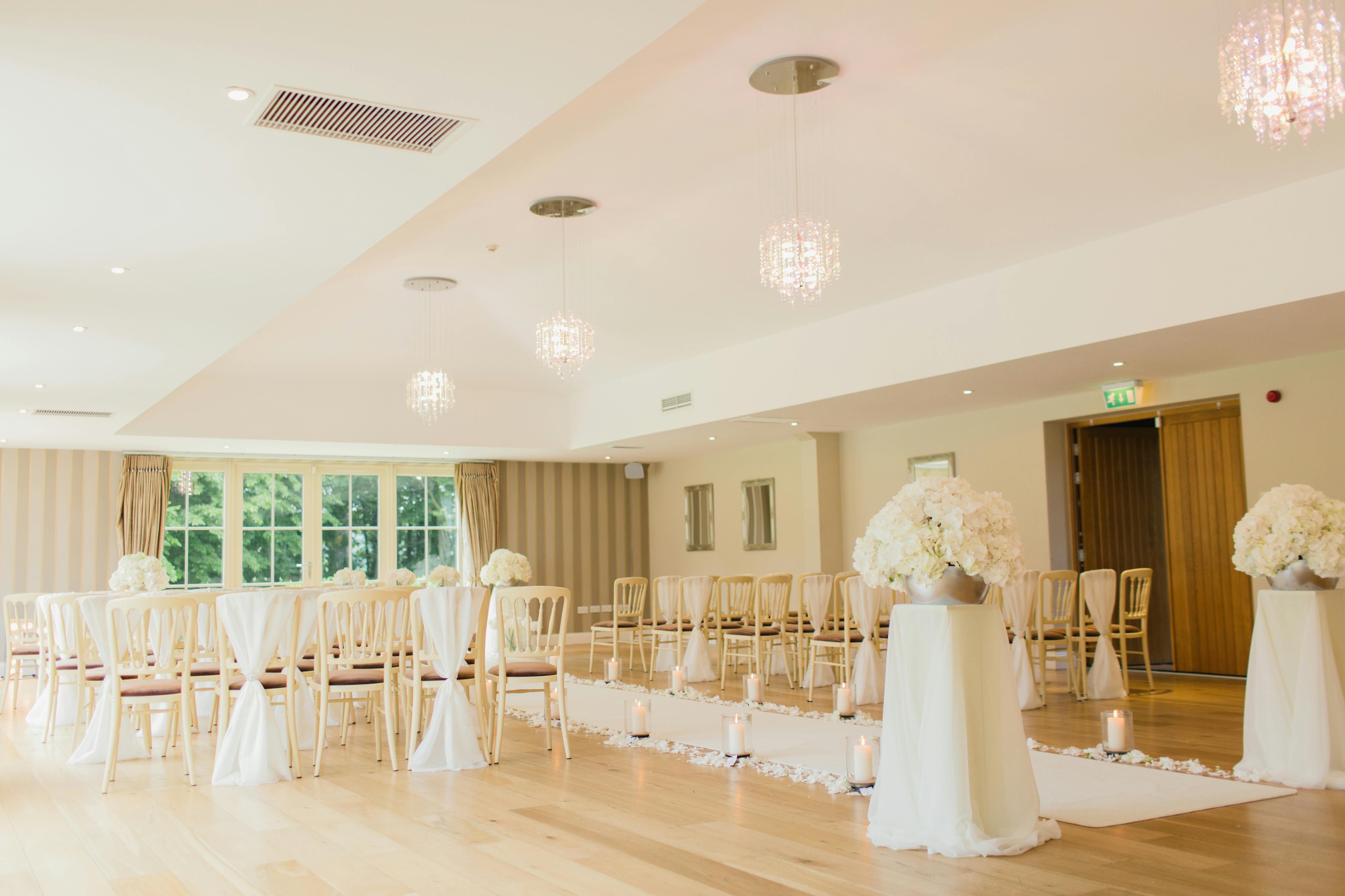 A wedding ceremony set up with a white runner, white florals, and white chairs.