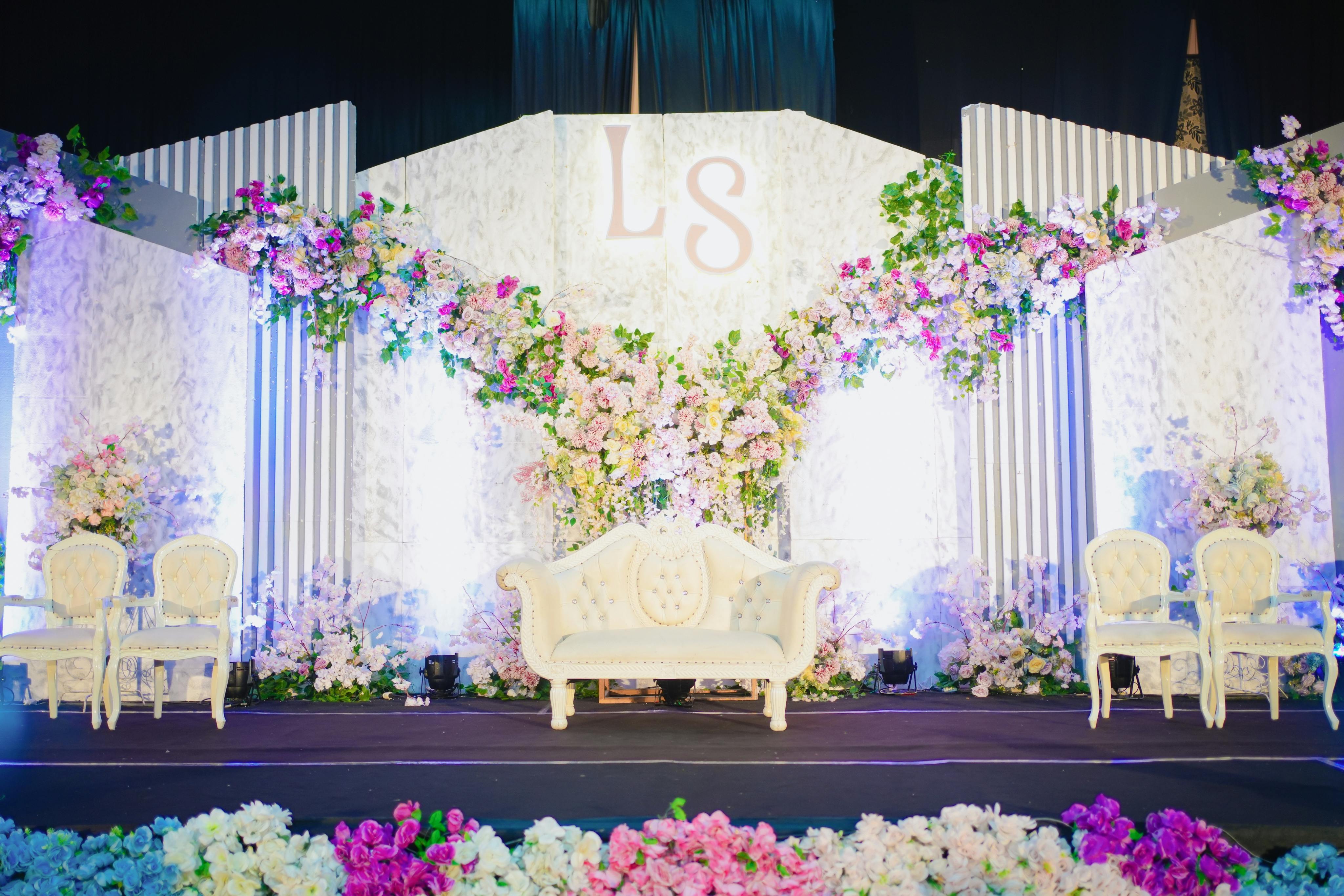 An elaborate floral backdrop with an ornate white sofa in the center and elegant white chairs set on either side.