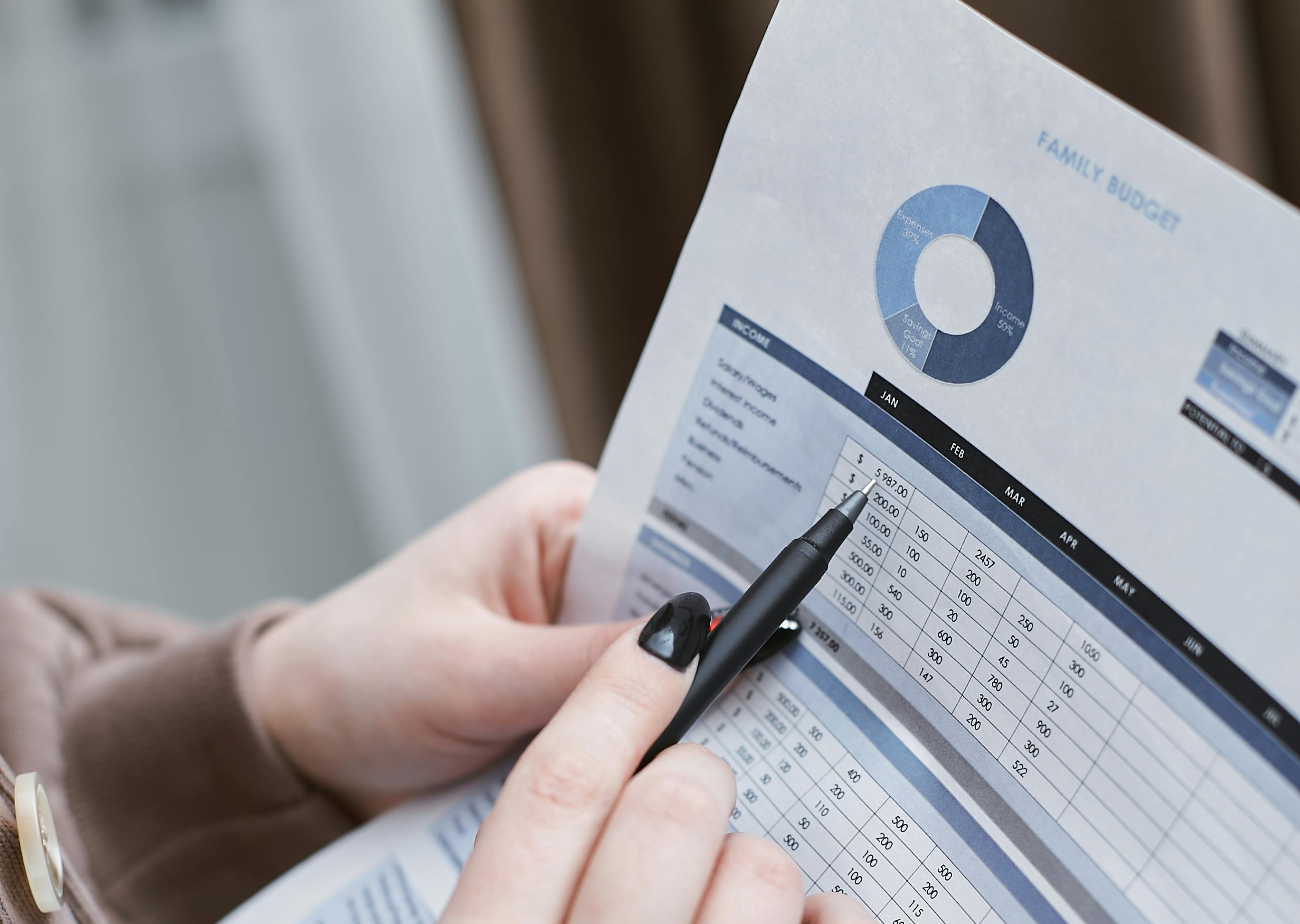 A pair of hands points at a printed budget with a pen.