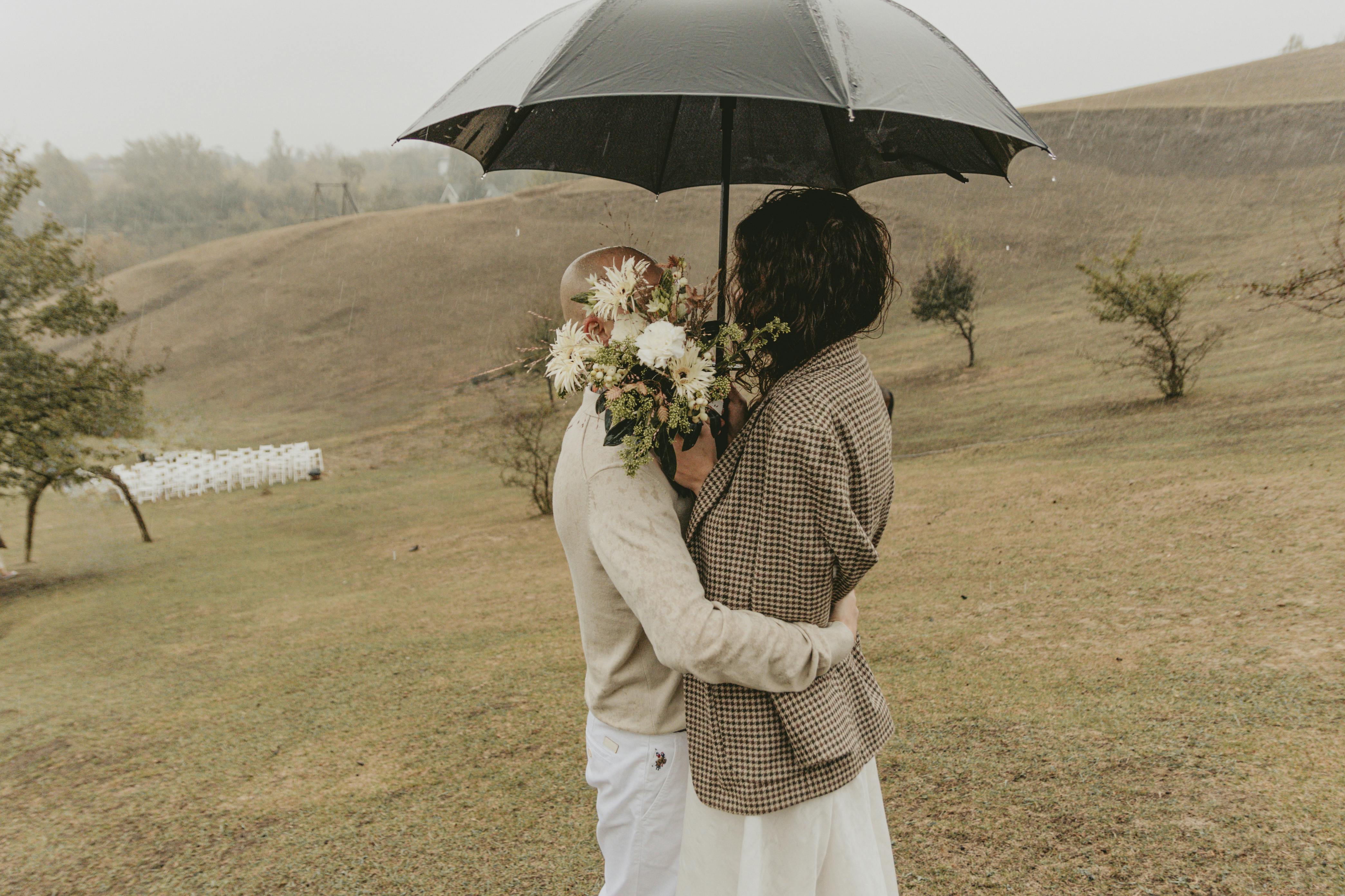 A couple embraces in the rain under an umbrella.