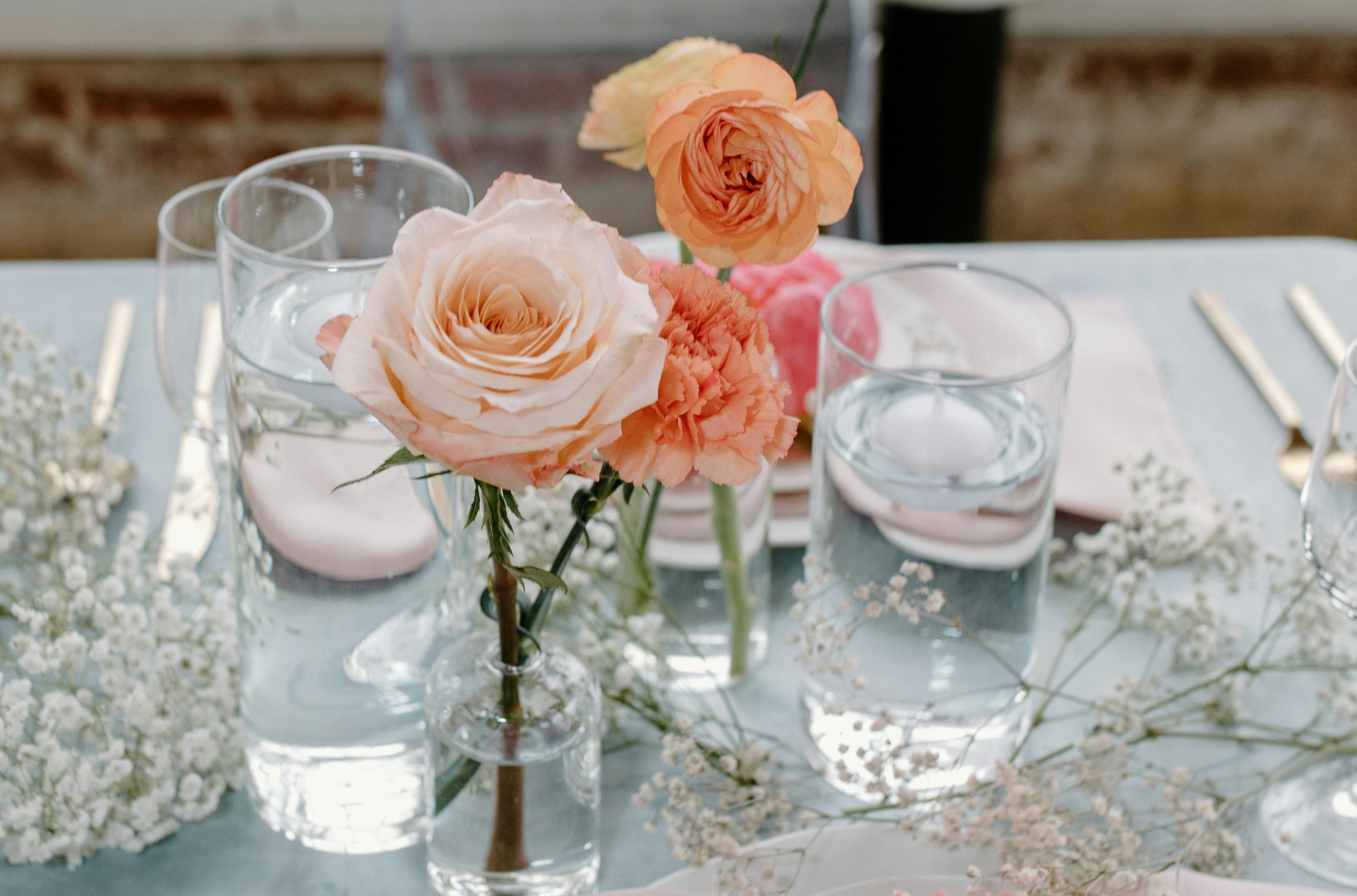 A simple centerpiece consisting of bud vases with pink and orange flowers, scattered baby's breath, and floating candles.