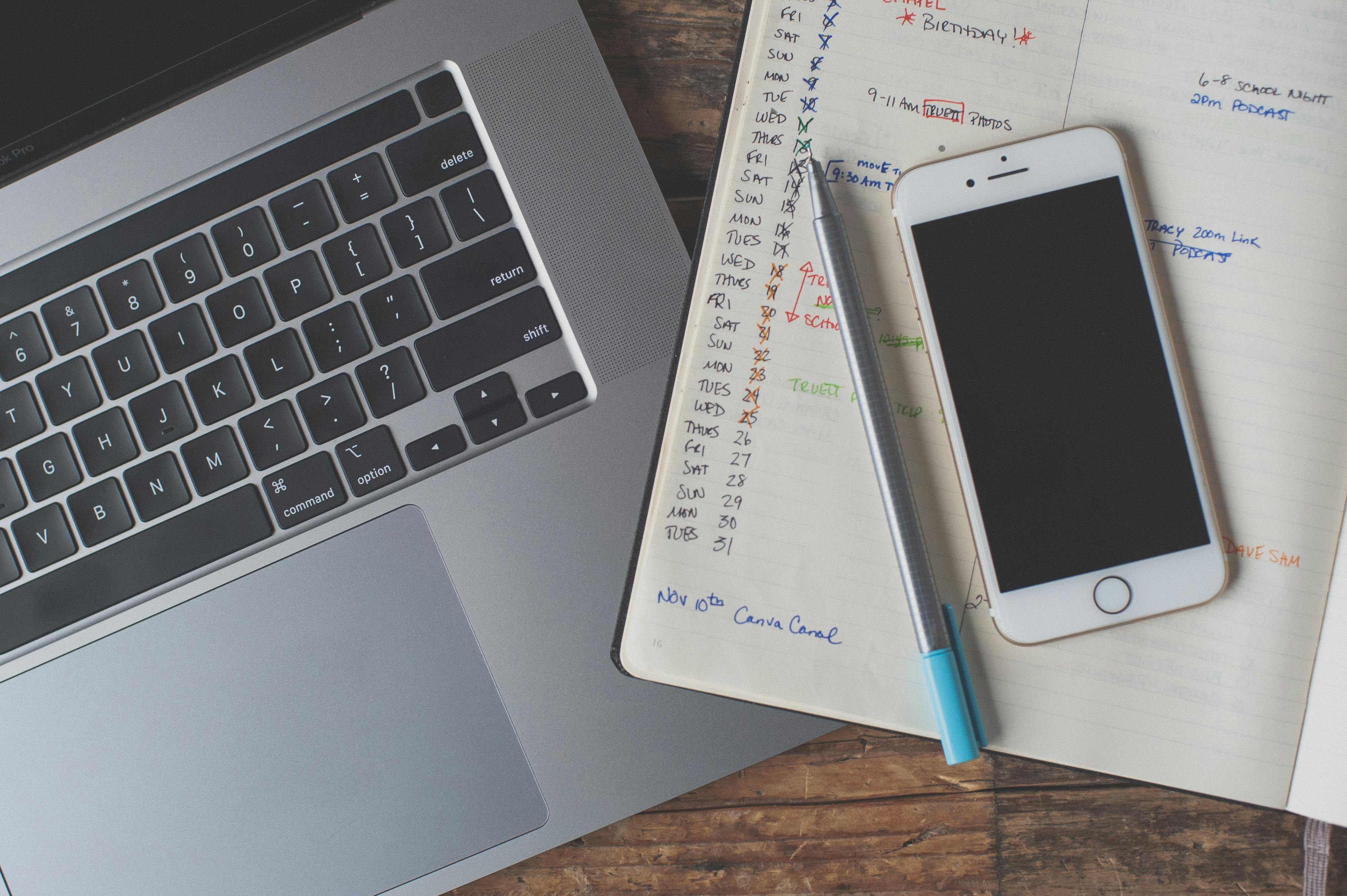 A laptop, notebook, pen, and cellphone laid on a desk.