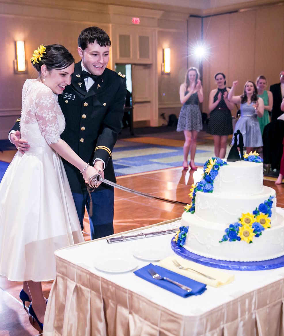 military husband and bride cutting cake with a sword